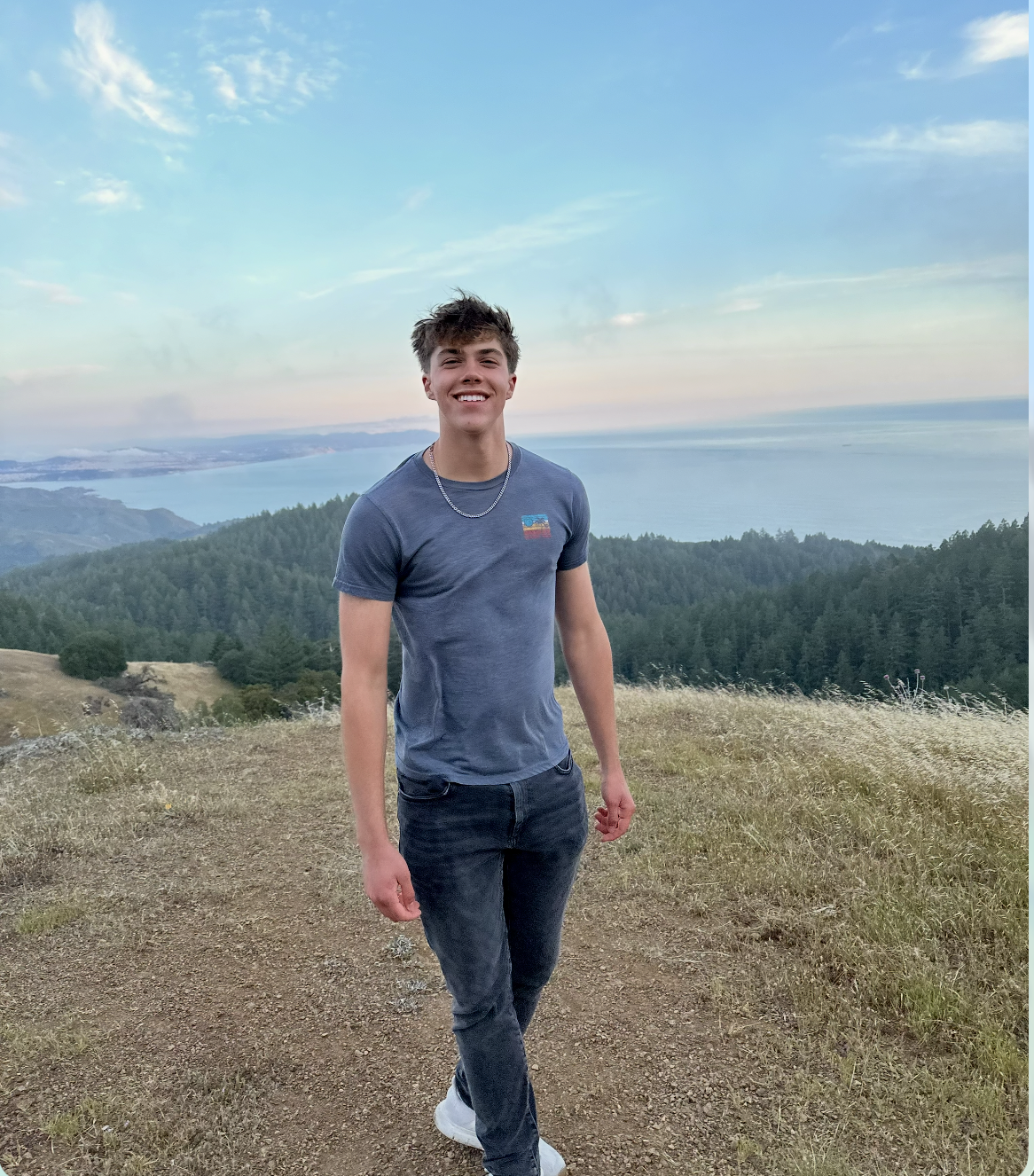 Luc Rulmont smiling outdoors with a coastal mountain and ocean landscape behind him